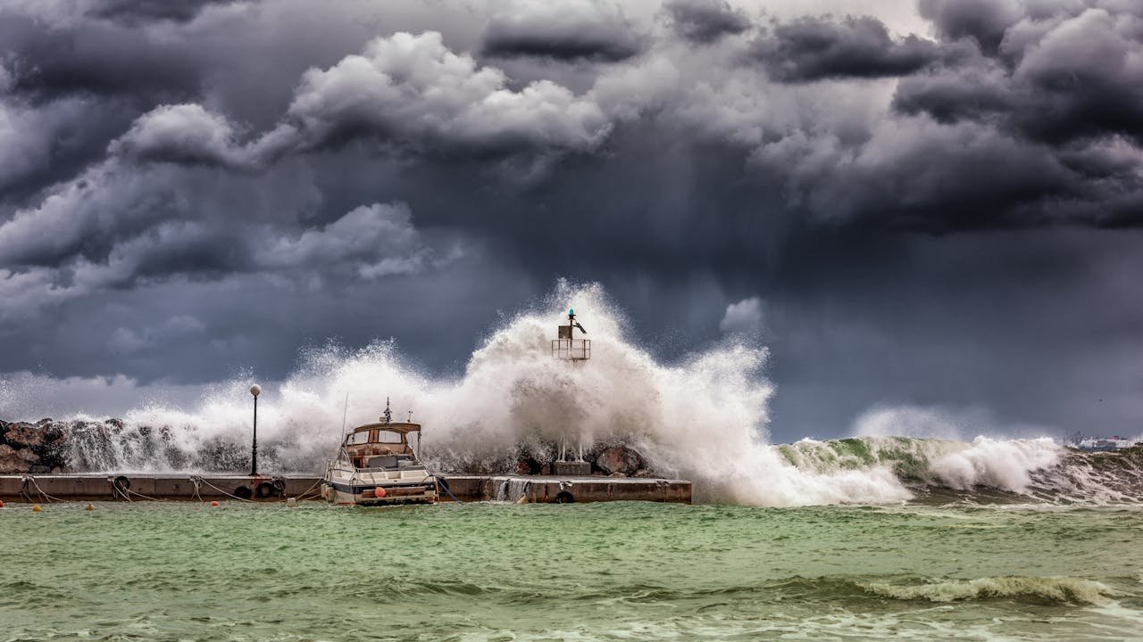 who-we-are Powerful waves crash against a pier and lighthouse under dark stormy skies.